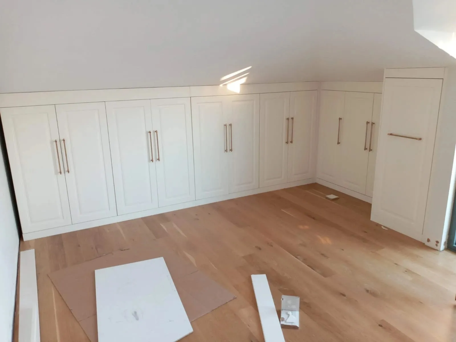 Zolderkamer met witte inbouwkasten langs de knieschotten
